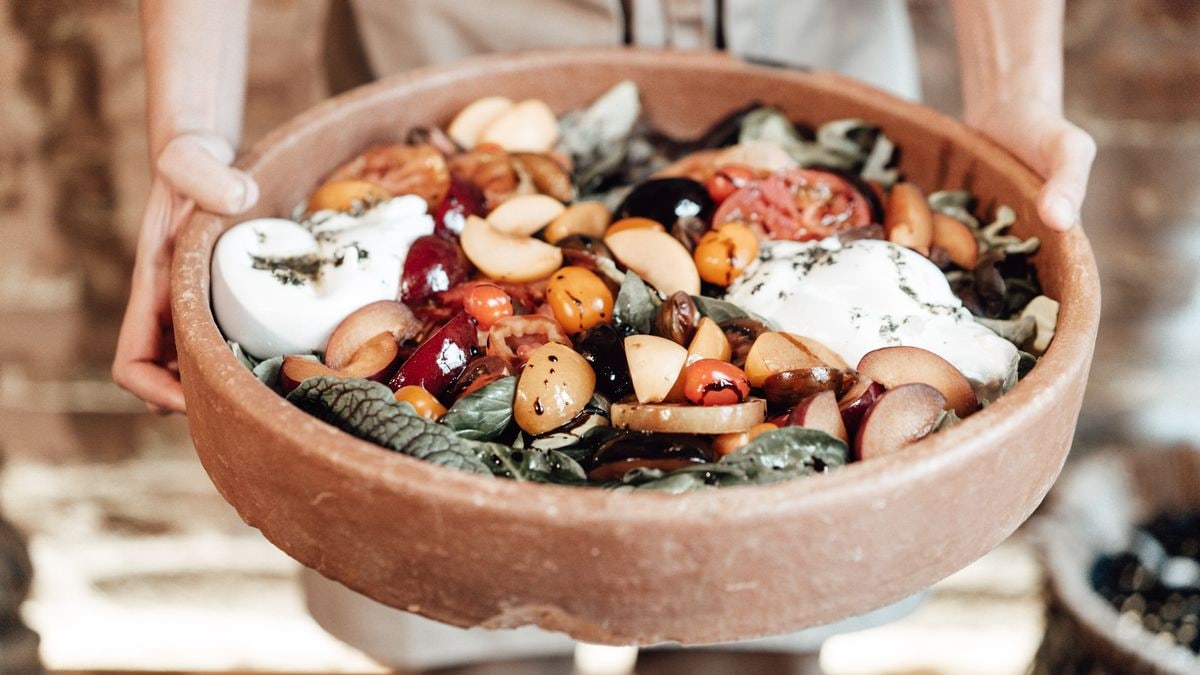 A vibrant rustic salad featuring fresh fruits, greens, and cheese in a wooden bowl, perfect for summer meals.